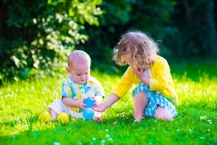 Two young children playing with balls in grass