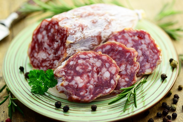 Sausage slices on a plate with rosemary and peppercorns