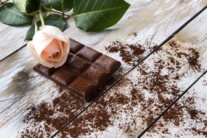 Chocolate bar with rose and cocoa powder on wooden table