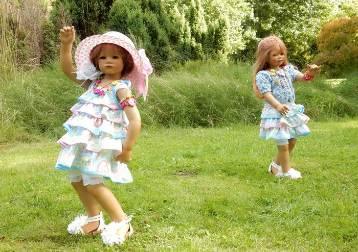 Two dolls in dresses and hats in a park