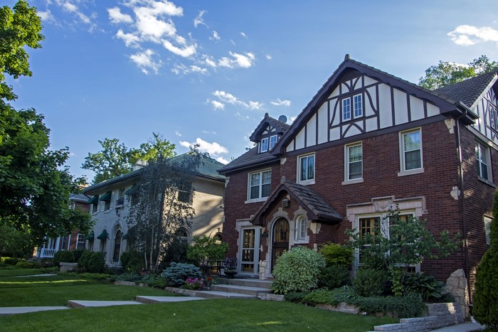 Two houses with lawns and trees under a blue sky