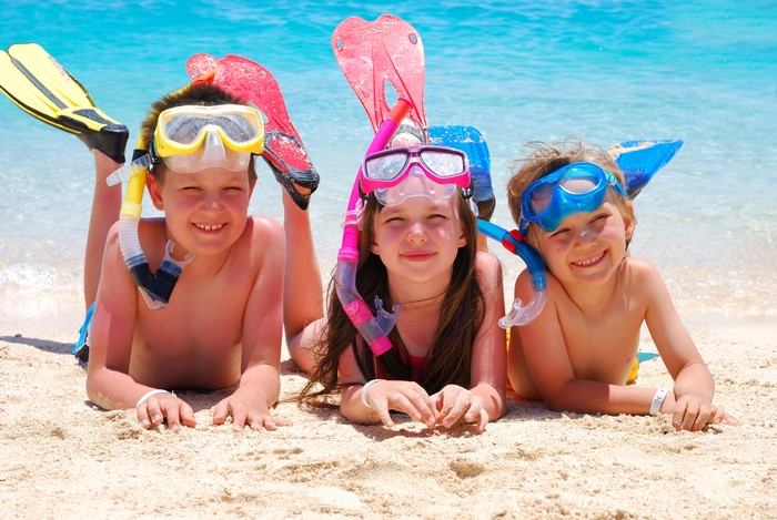 Three children with snorkeling gear on a beach