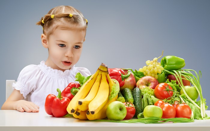 Little girl looking at a pile of fruits and vegetables
