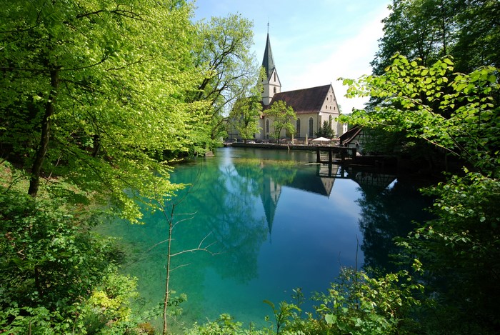 Church reflected in a clear blue lake in Blaubeuren, Germany