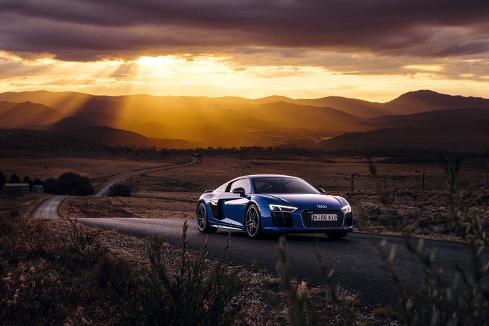 Blue Audi R8 V10 Plus on a winding road at sunset
