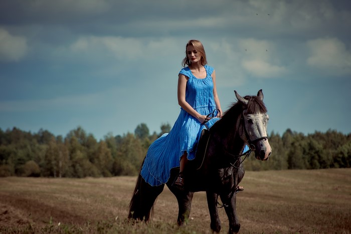 Blonde girl in blue dress riding a horse