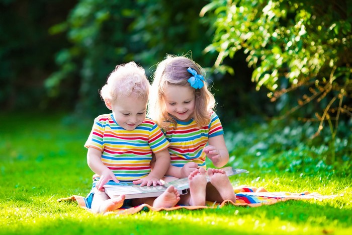 Two children reading a book on a blanket in the grass