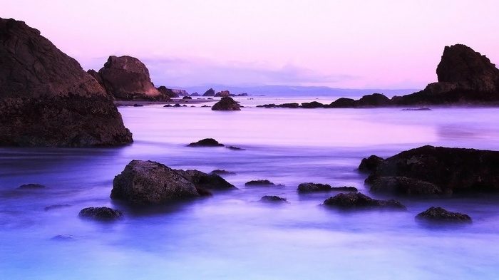Ocean rocks at sunset with purple and pink sky
