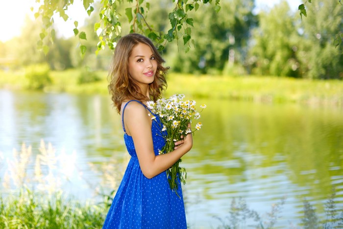 Brown-haired girl in blue dress holding camomile bouquet