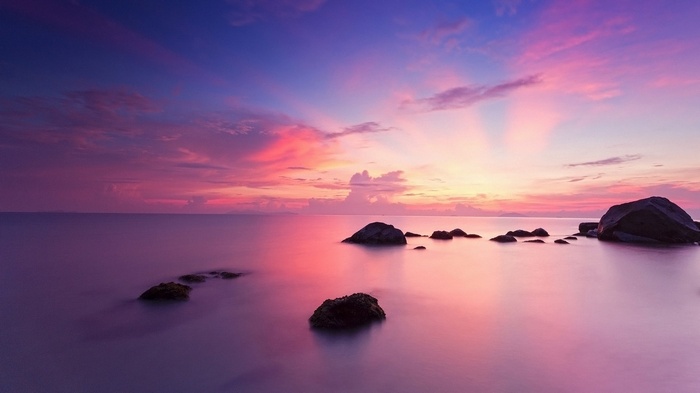 Ocean sunset with pink and purple clouds and rocks