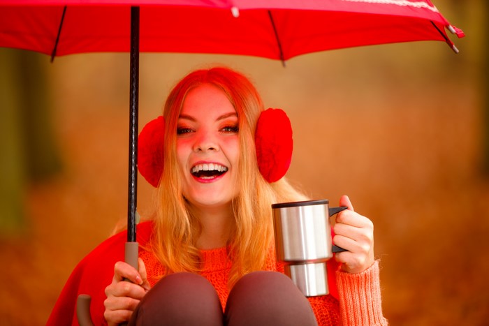 Blonde girl with headphones holding a mug under an umbrella