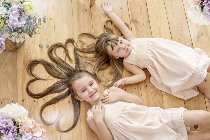 Two little girls with long brown hair lying on wooden floor