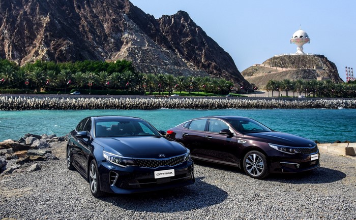 Two Kia Optima cars by the sea with mountains