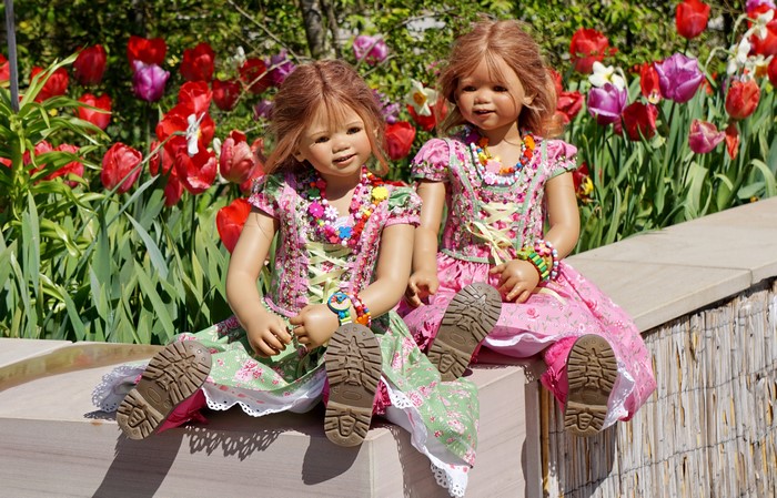 Two dolls in dresses sitting in front of tulips