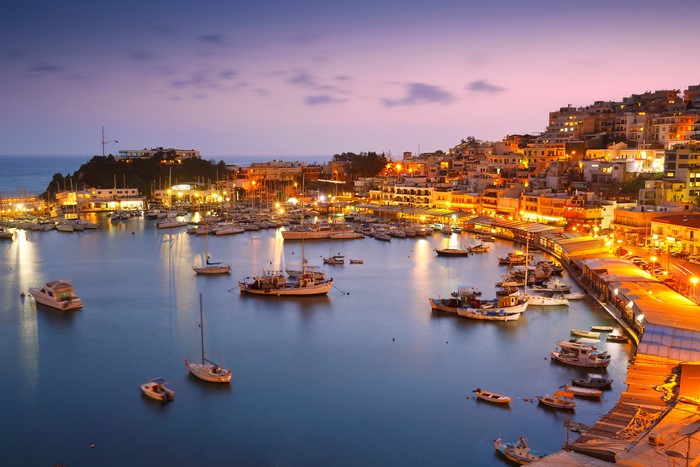 Harbor with boats and illuminated buildings at dusk in Greece