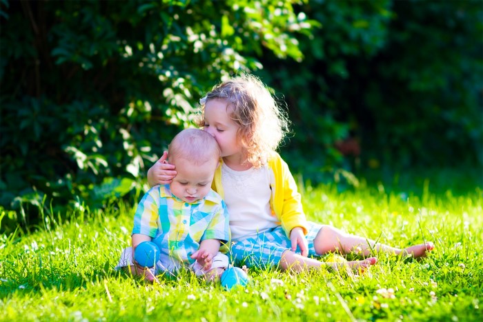 Girl kissing baby brother on grass