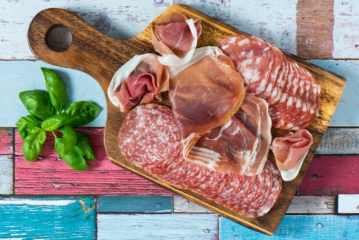 Meat products on a wooden board with basil