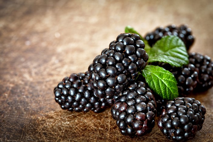 Blackberries with green leaves on a wooden surface
