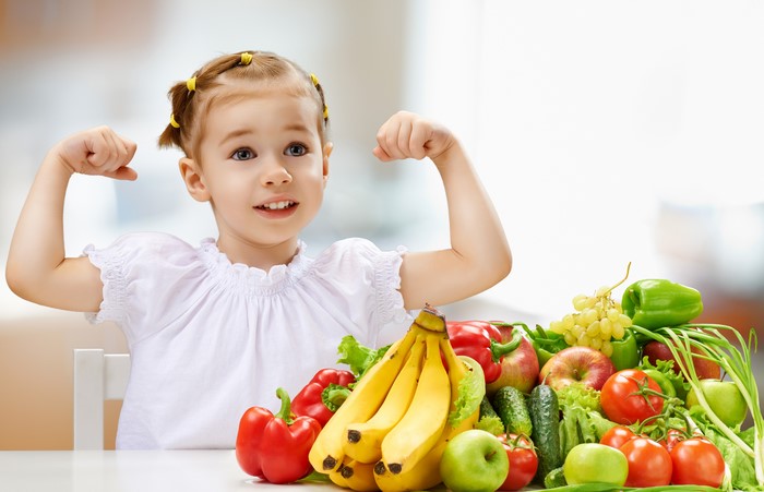 Little girl flexing with fruits and vegetables