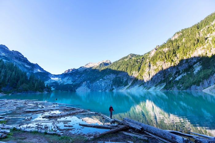 Person standing on logs in a turquoise lake with mountains