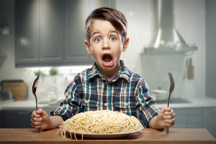 Boy with a plate of pasta and cutlery