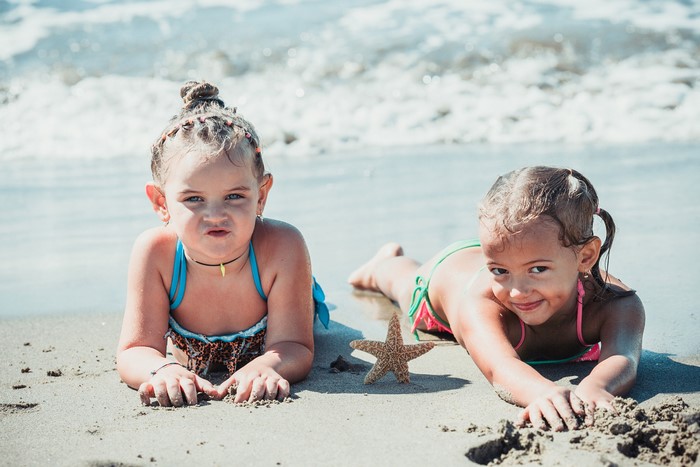 Two young girls lying on a sandy beach