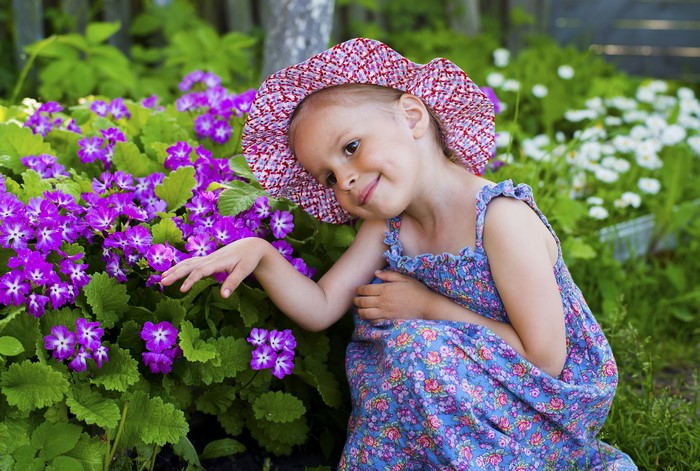 Little girl in a hat and dress near purple flowers