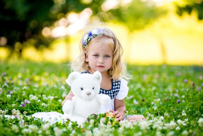 Young blonde girl holding a teddy bear in a field