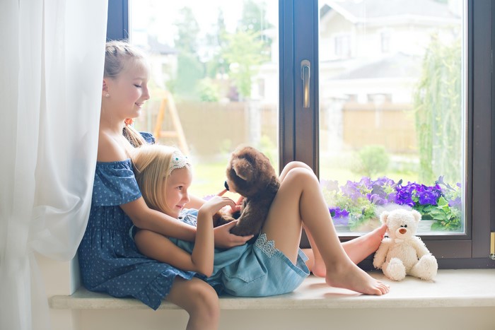 Two little girls with teddy bears by the window