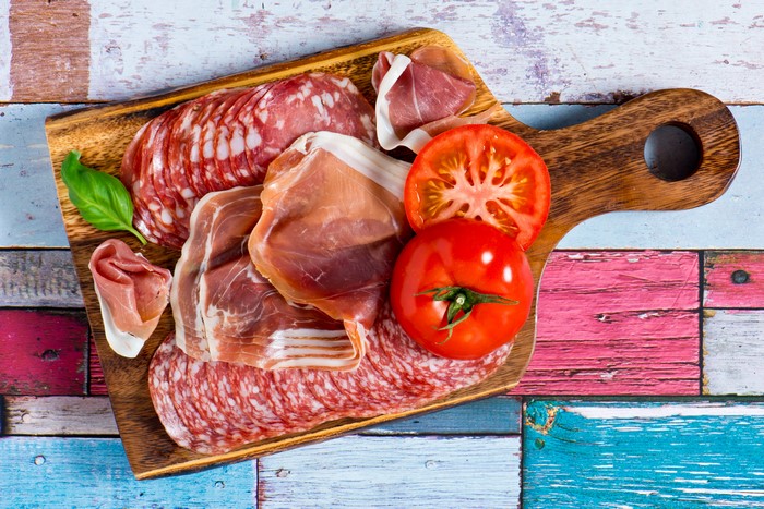 Meat products, sausage, ham, and tomatoes on a cutting board