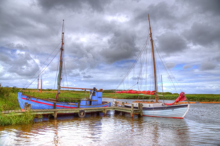 Boats docked on a river under a cloudy sky