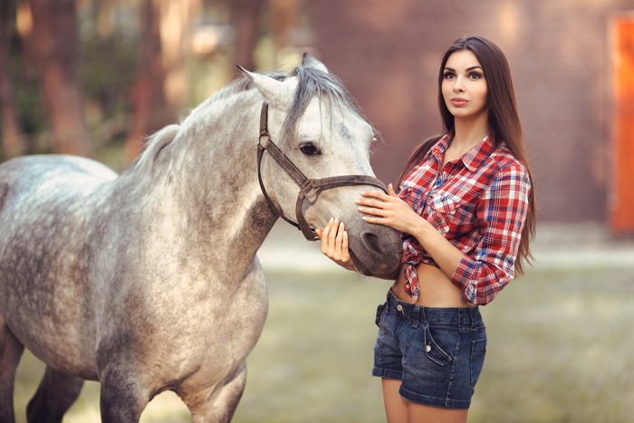Woman in plaid shirt and denim shorts with a horse