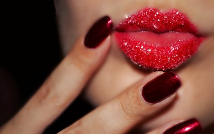 Close-up of lips with sugar and red manicure