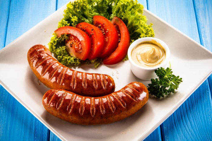 Two Vienna sausages with tomatoes, lettuce, and mustard