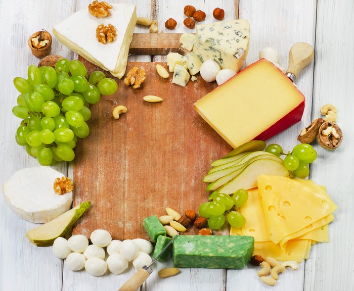 Cheese platter with grapes, nuts, and pears on a cutting board