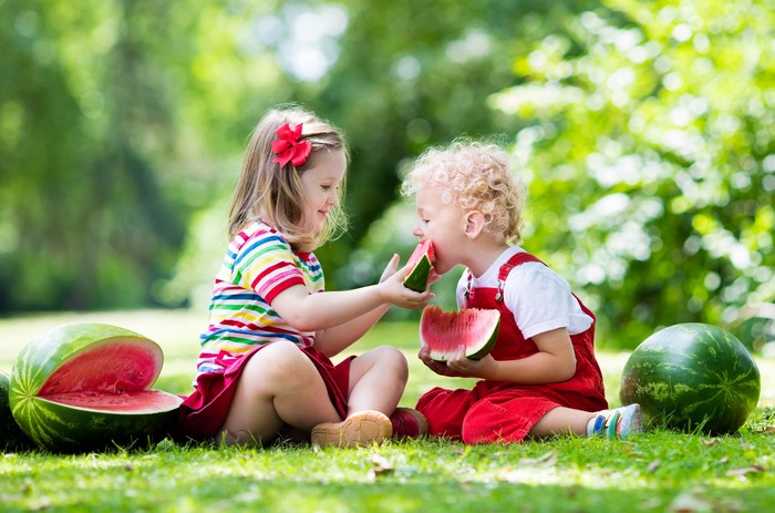 Two children eating watermelon in a park