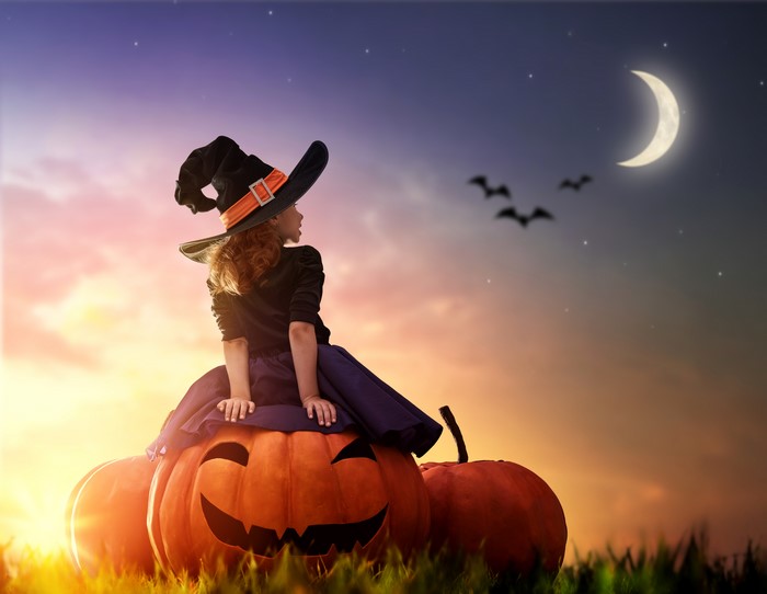 Girl in witch hat on pumpkins at Halloween night