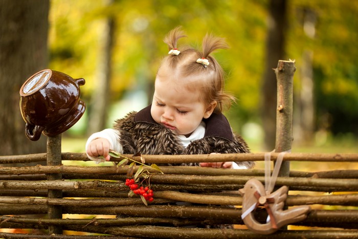 Little girl in fur vest by a wooden fence