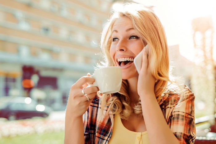 Blonde girl laughing while holding a coffee cup and talking on the phone