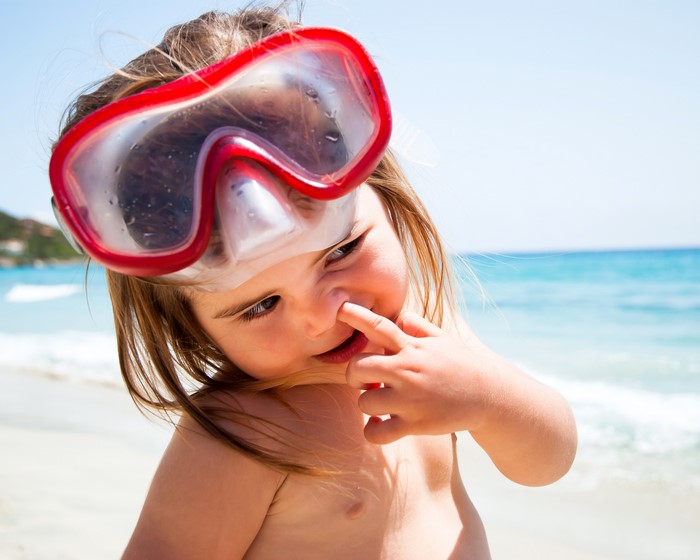 Girl with snorkel mask picking her nose on the beach