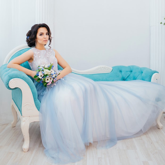 Brunette woman in a blue dress holding a bouquet on a sofa
