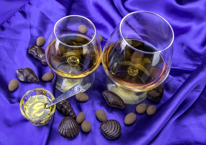 Two glasses of brandy with chocolates and almonds on purple silk