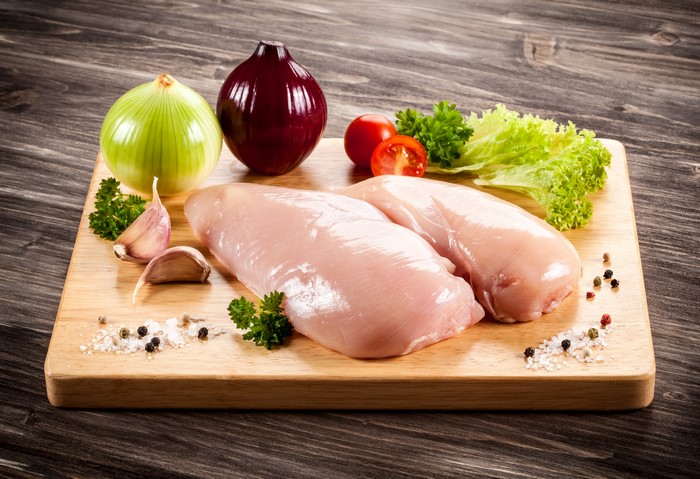 Raw chicken breasts with vegetables and spices on a cutting board