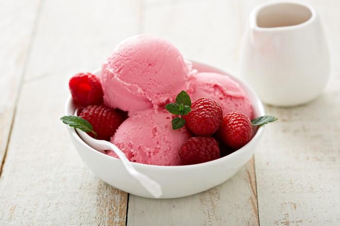 Raspberry ice cream in a bowl with fresh raspberries