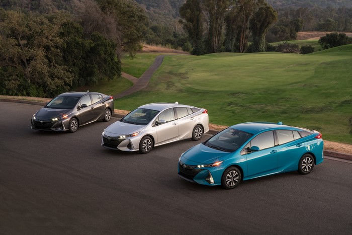 Three Toyota Prius cars on a road with a golf course background