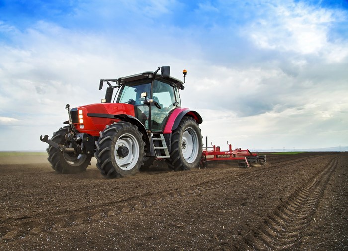 Red tractor plowing a field under a cloudy sky