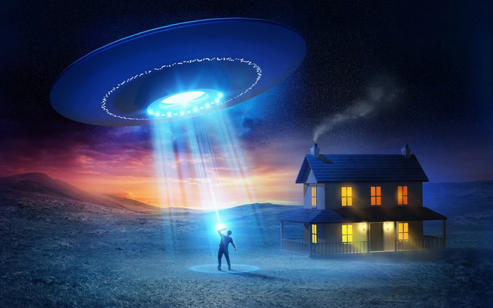 UFO hovering over a house with a person in a light beam