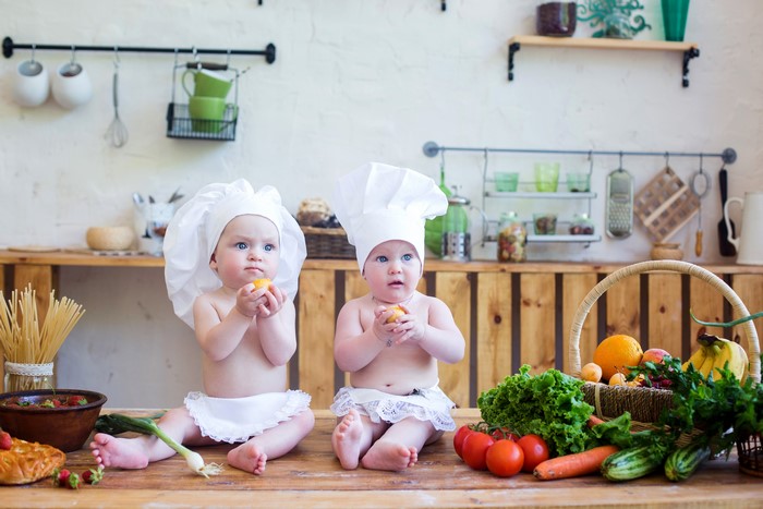 Two babies dressed as chefs in a kitchen