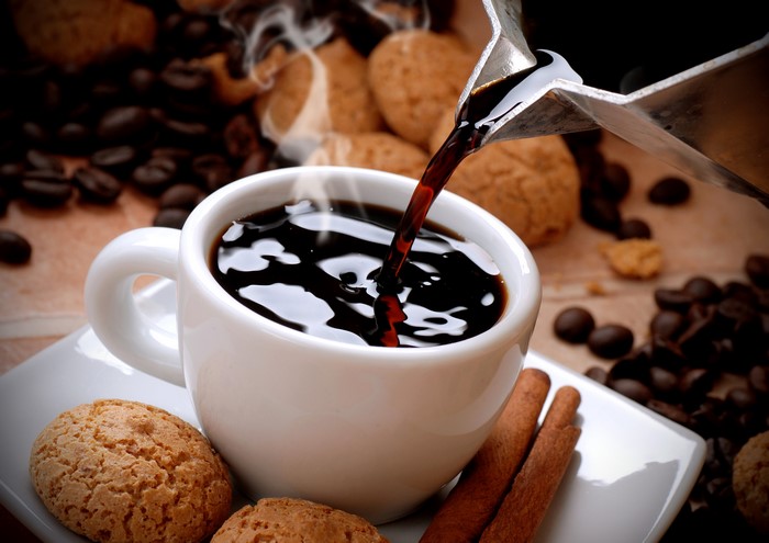 Coffee being poured into a cup with cookies and cinnamon sticks