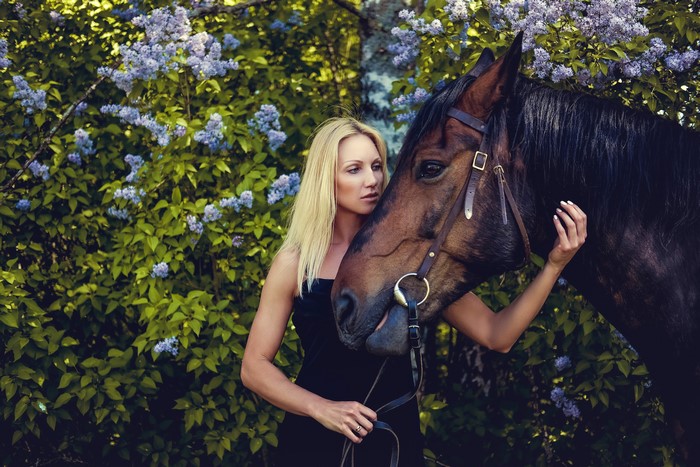 Blonde woman with a horse near lilac bushes